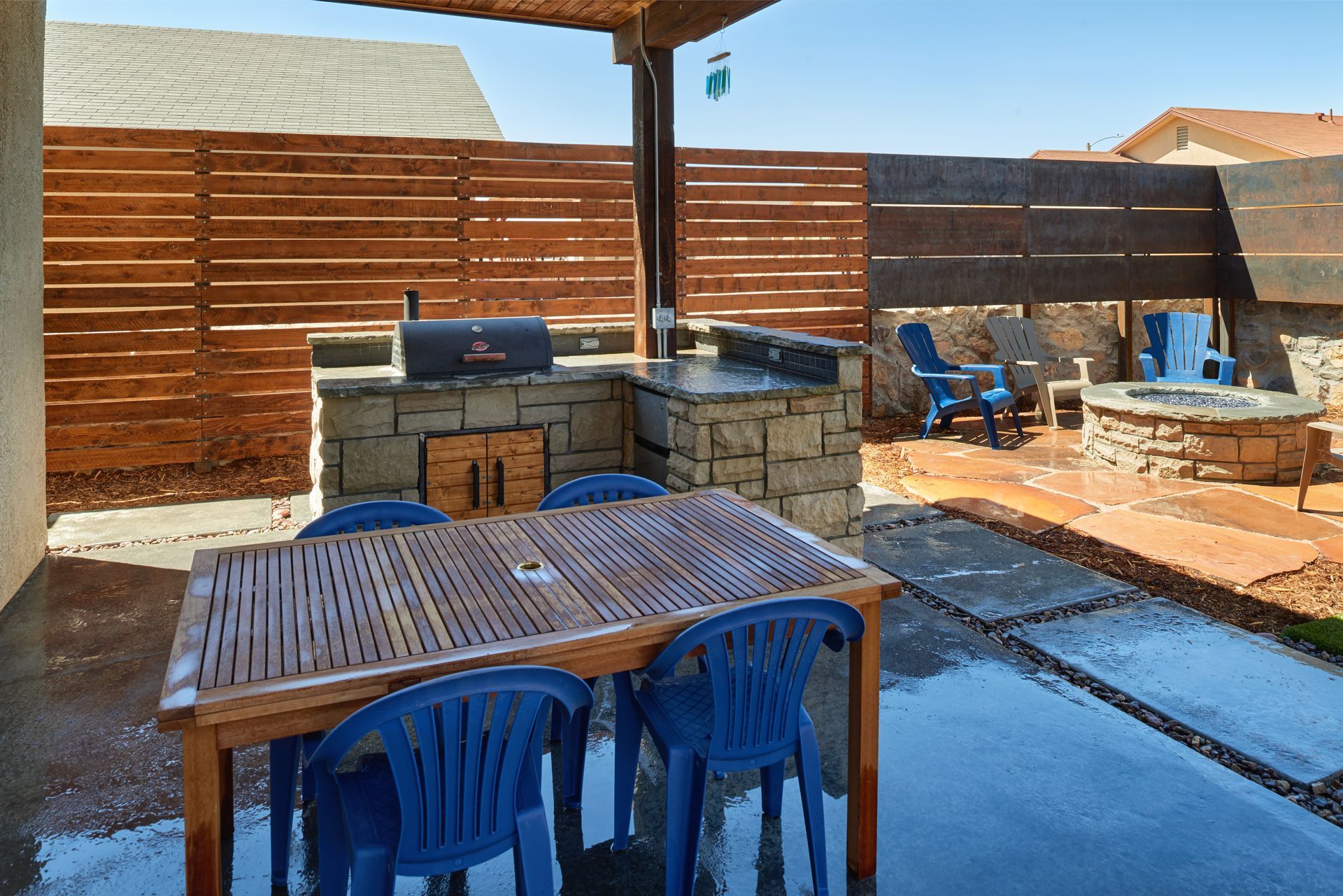 Patio with wooden table, blue chairs, built-in grill, fire pit, and horizontal wood fence.