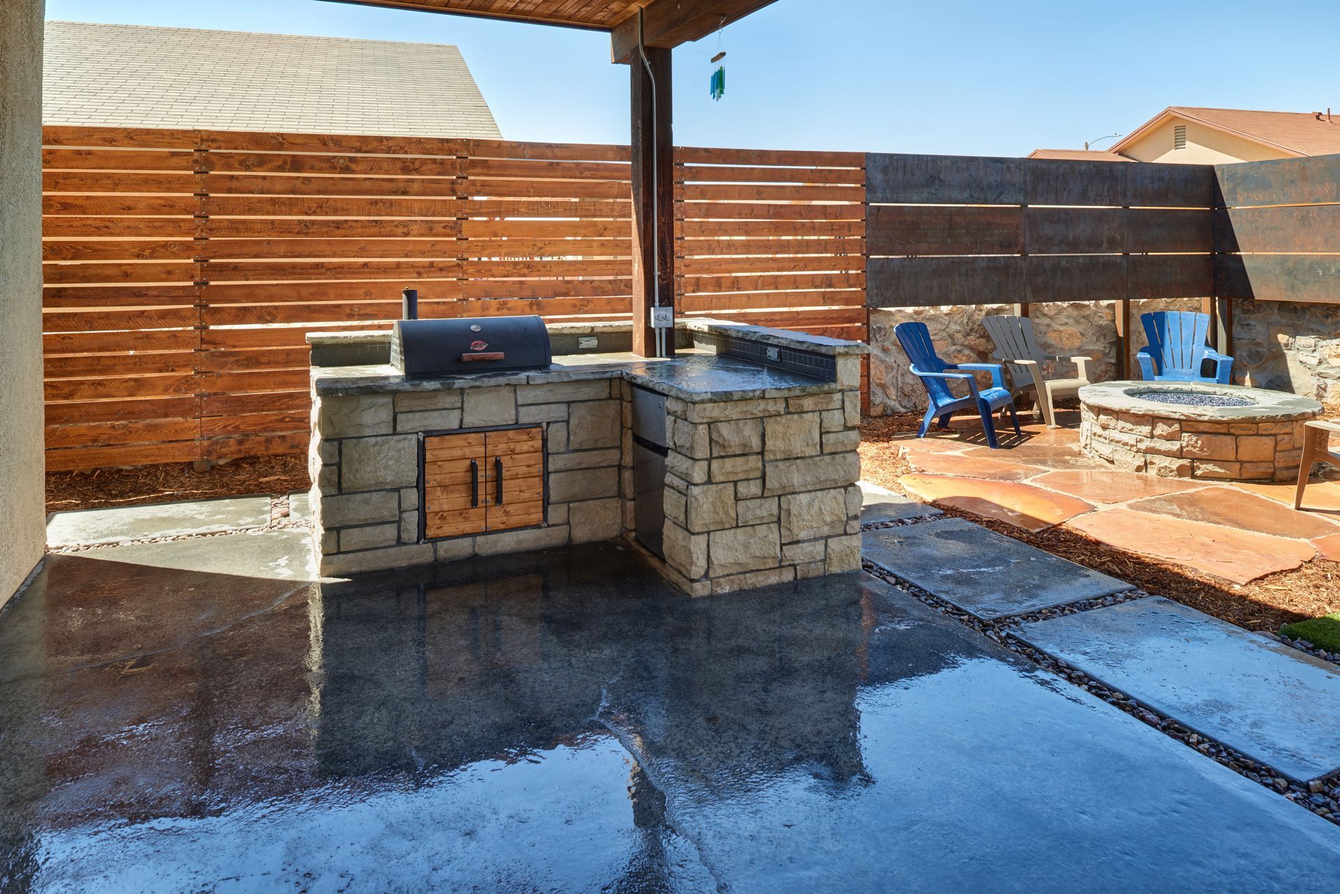 Outdoor kitchen with a grill, stone facade, and a fire pit.