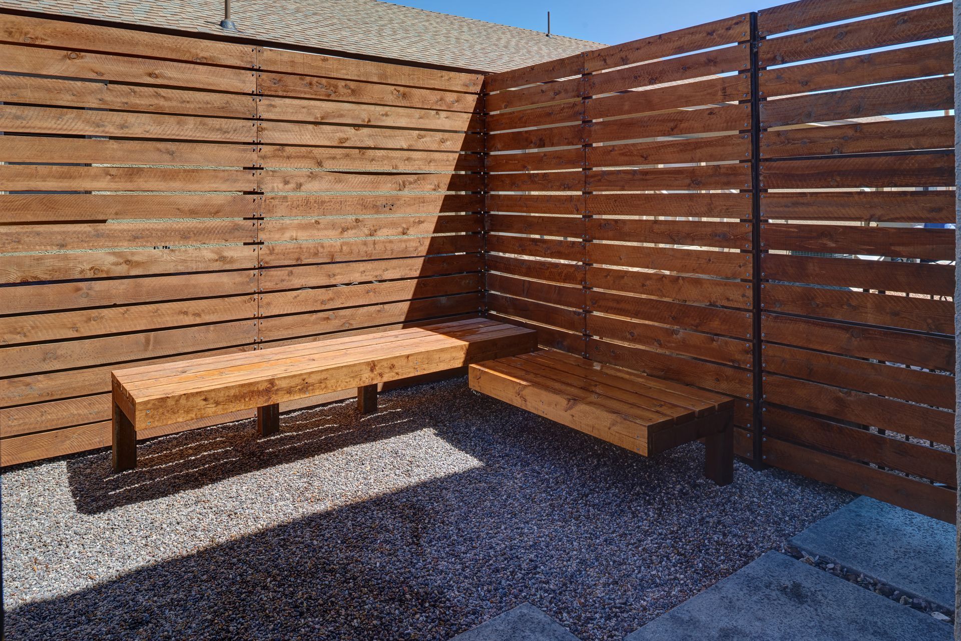 Two wooden benches on gravel within a wood slat fence enclosure.