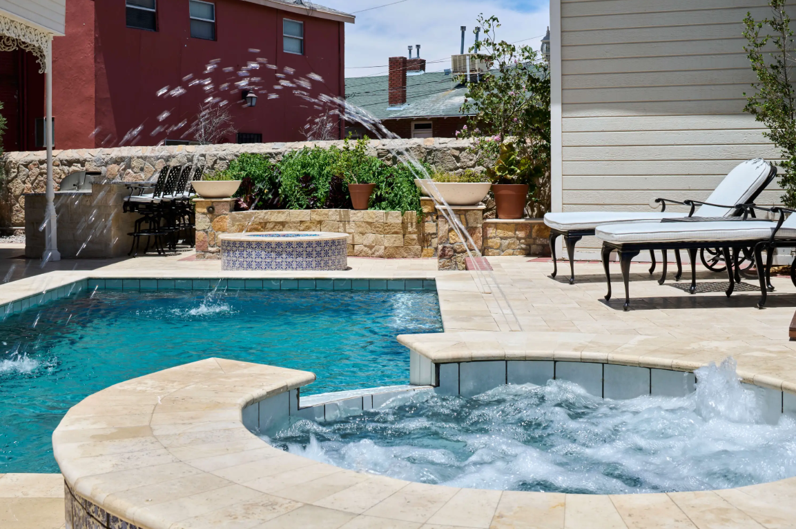 Swimming pool and hot tub with water features, surrounded by a patio and stone wall.