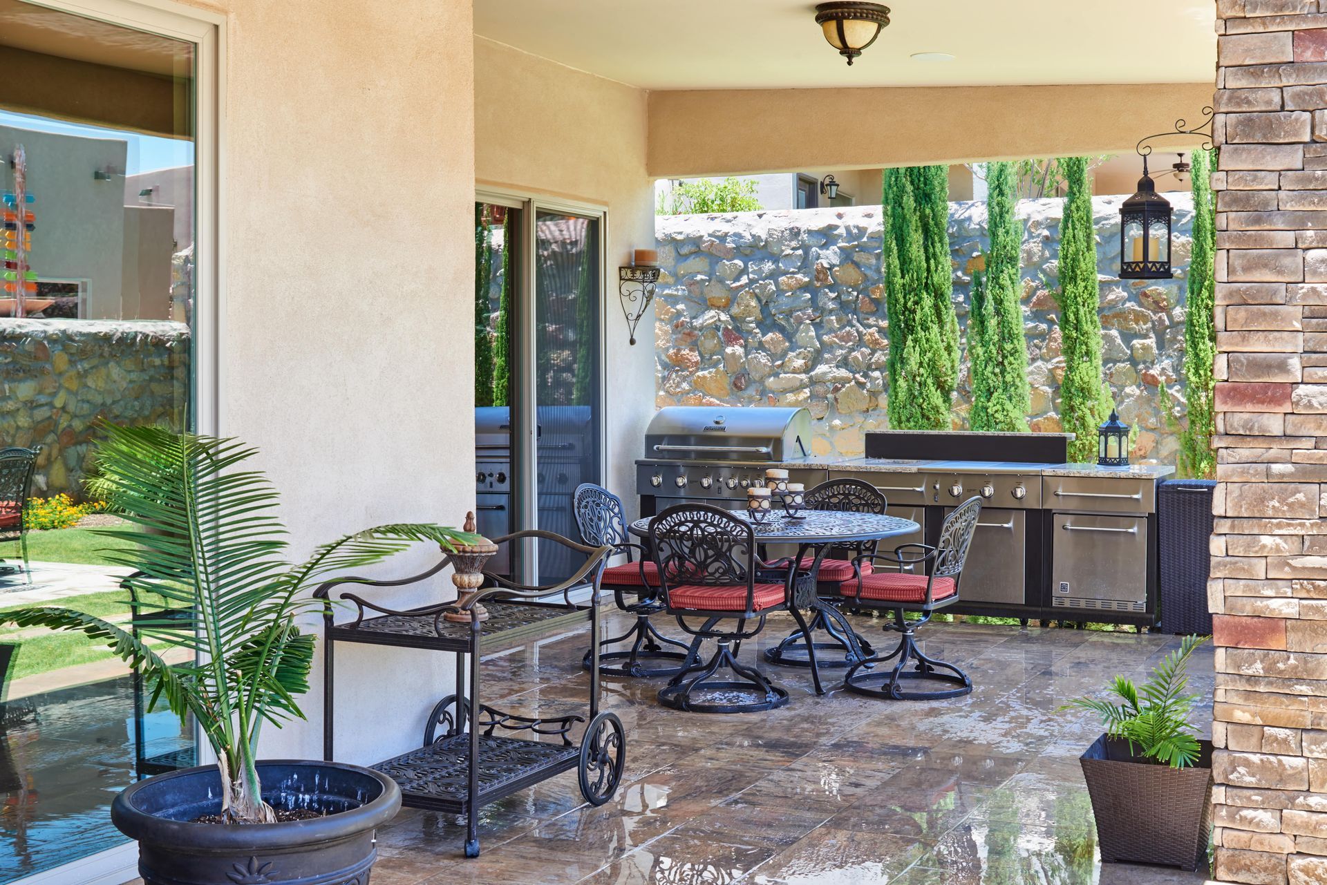 Patio with grill, table and chairs, potted plants, and stone wall backdrop.