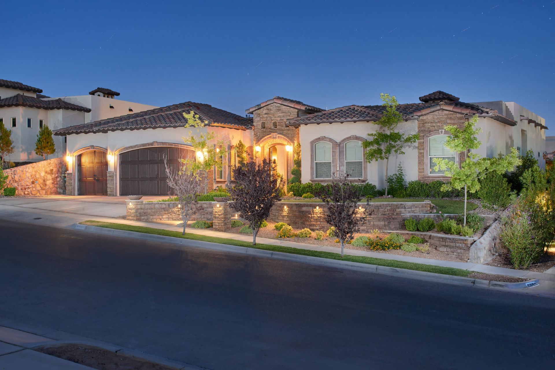 Upscale home with a stucco exterior, brick accents, and a tiled roof, lit at dusk.