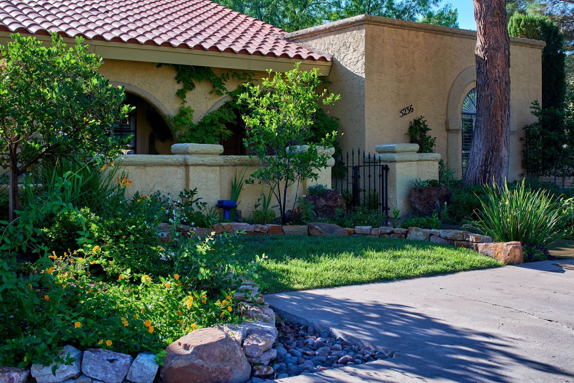Spanish-style home with a red-tiled roof and lush landscaping. A curving driveway leads to the house.