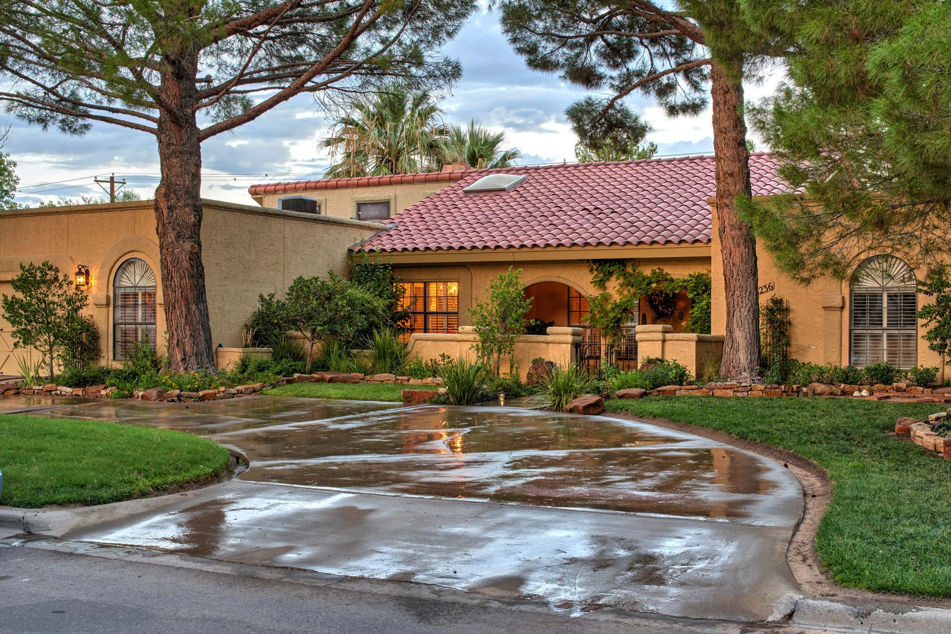 Spanish-style home with red-tile roof, trees, and wet driveway.