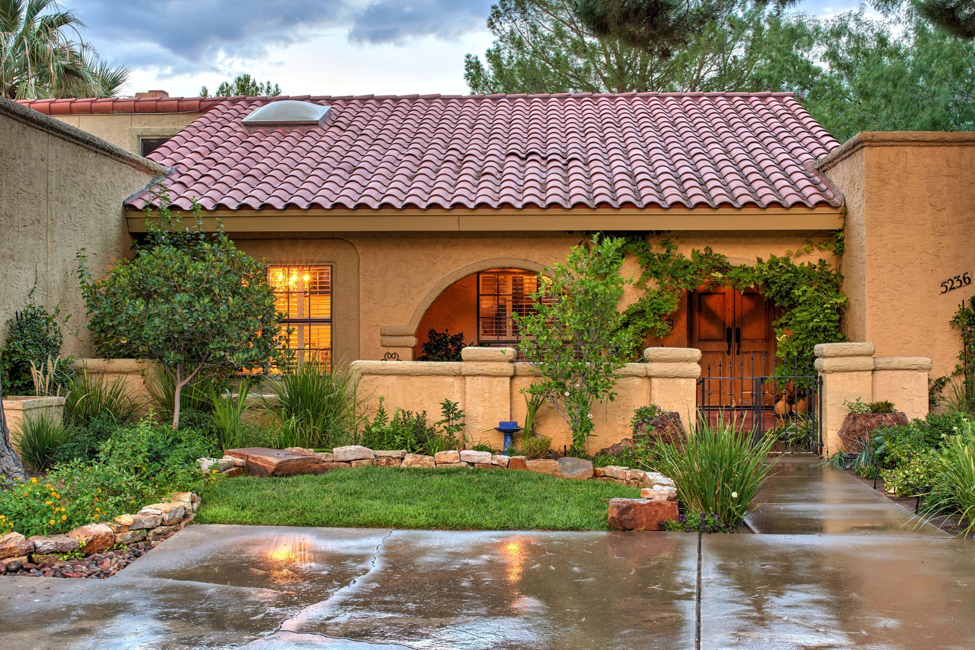Spanish-style home with red tile roof, arched doorway, and lush landscaping.