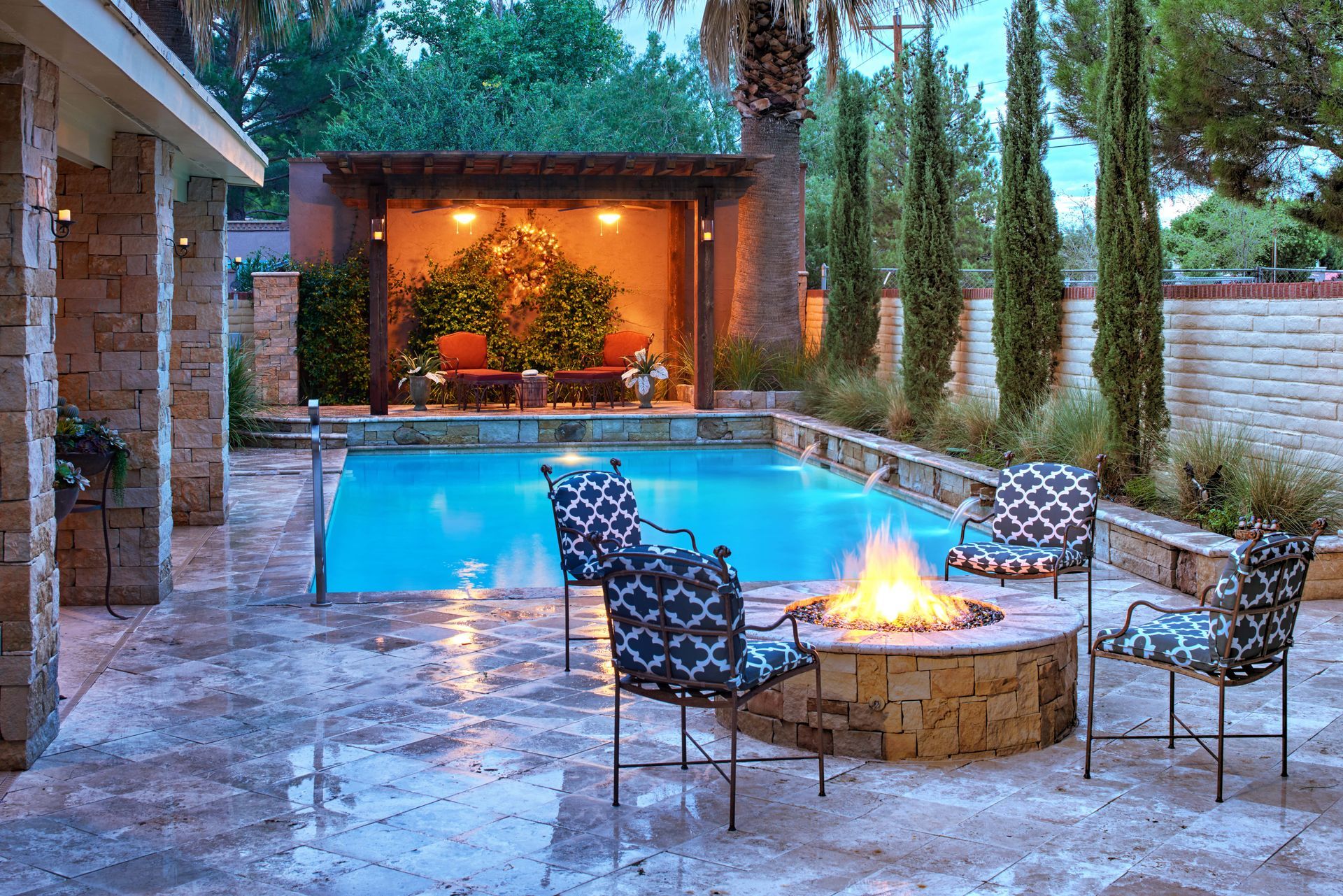 Backyard pool and fire pit with seating. Stone patio, pergola, and lush landscaping.