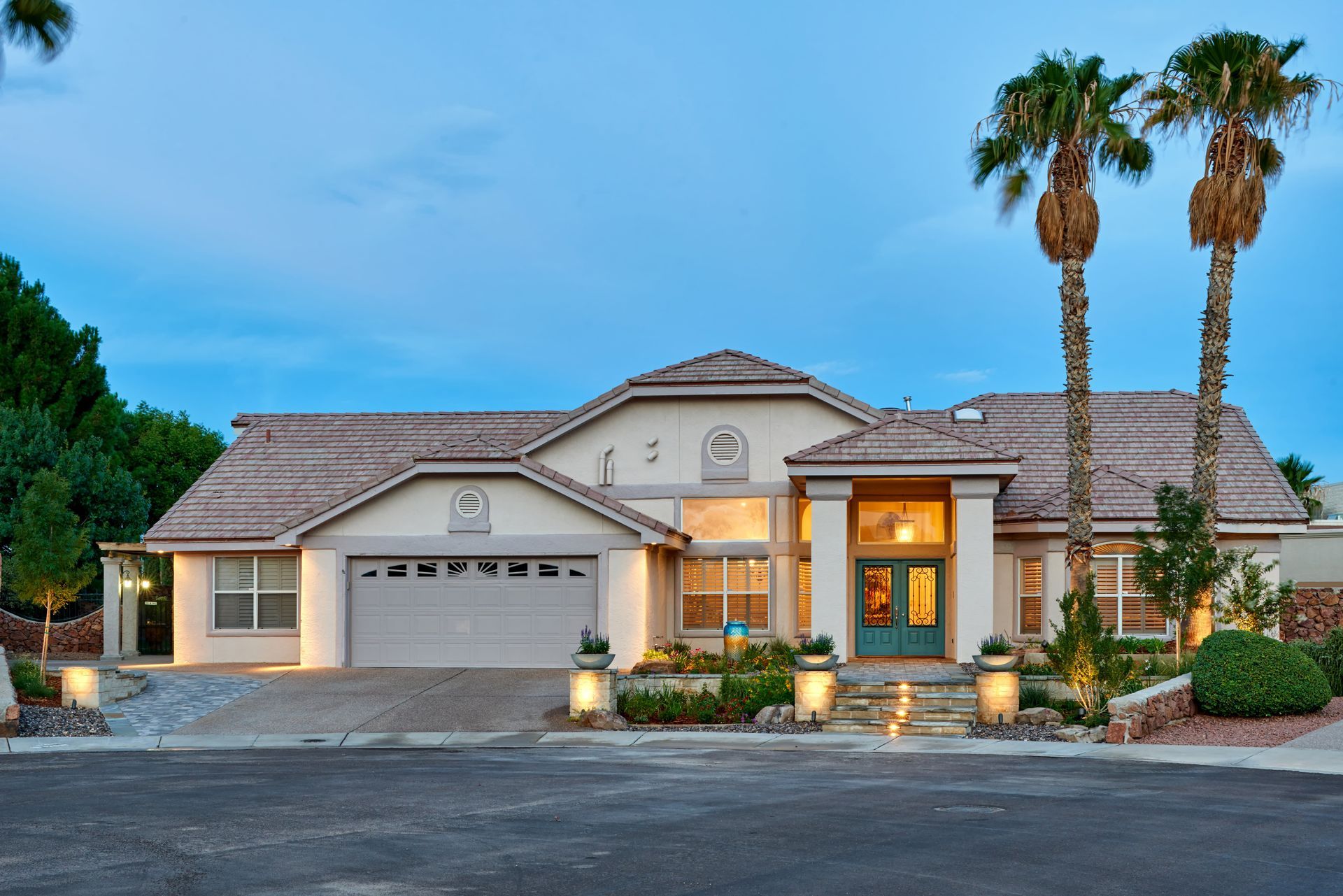A two-story beige house with a turquoise door, palm trees, and a blue sky.