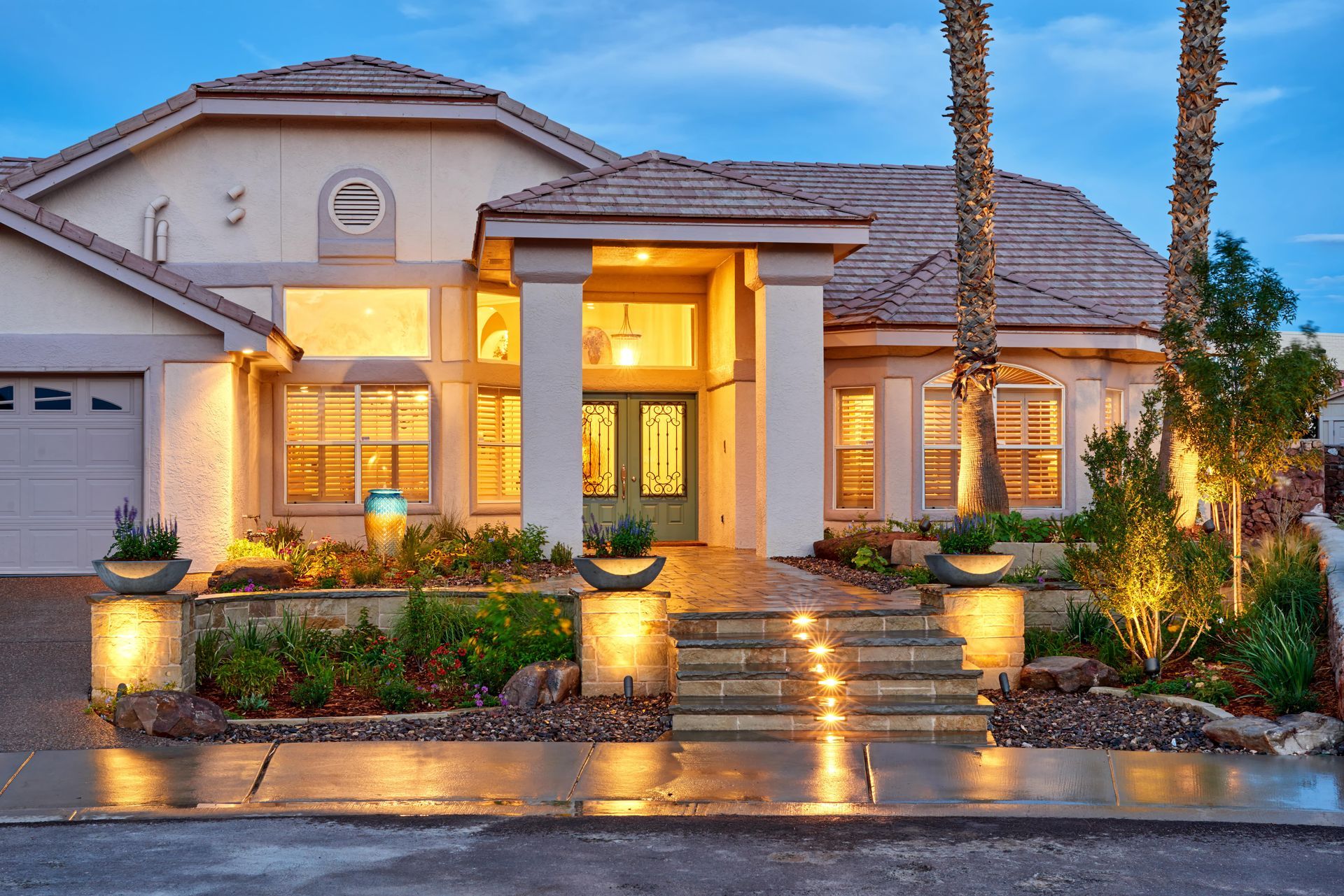 House exterior at dusk, illuminated entrance with steps and landscaping, palm trees.