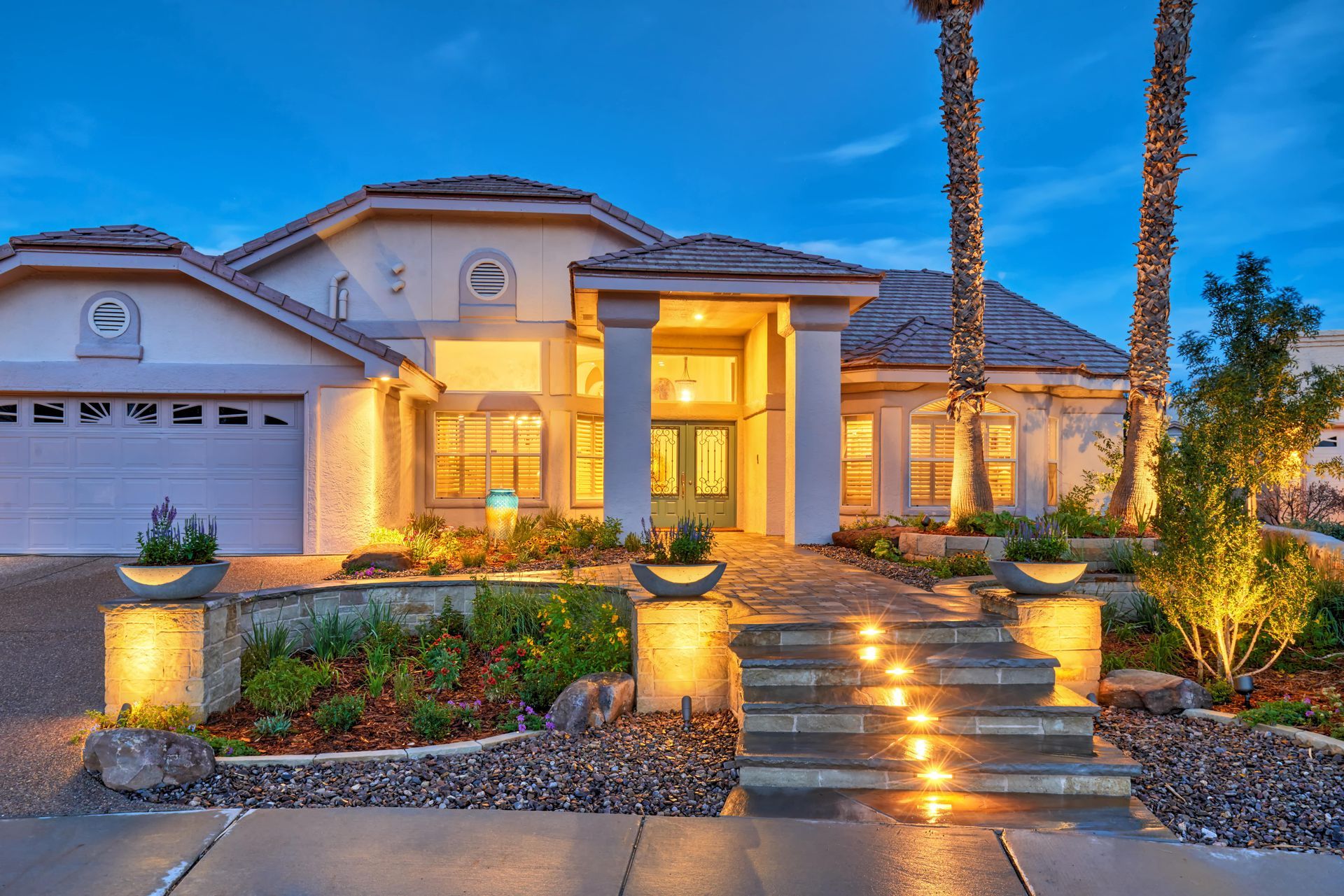 Elegant house exterior with illuminated steps, pillars, and landscaping at twilight.