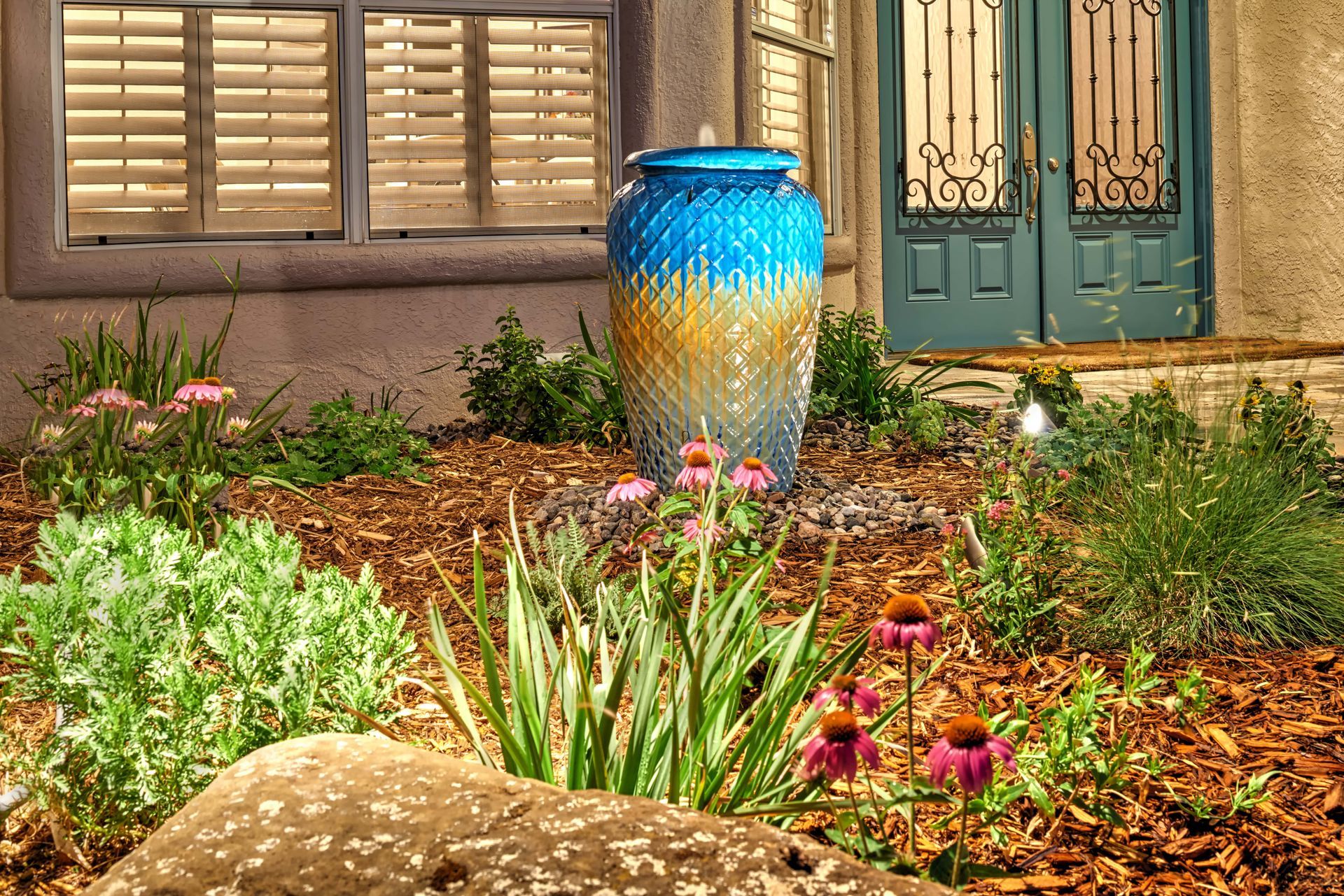 Blue and gold decorative fountain in a garden bed with blooming pink flowers.