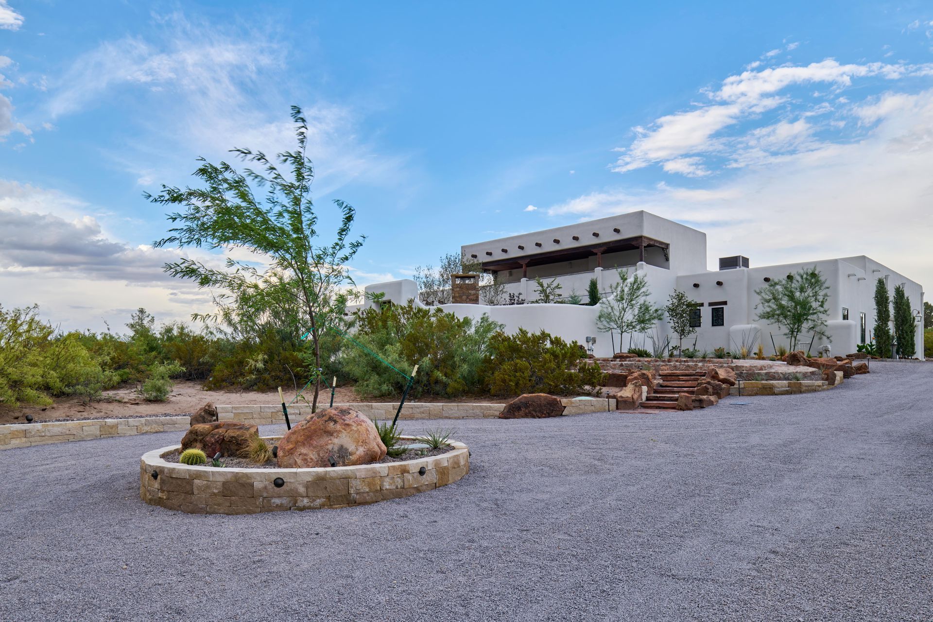 White stucco house with a flat roof, surrounded by desert landscaping and gravel drive.