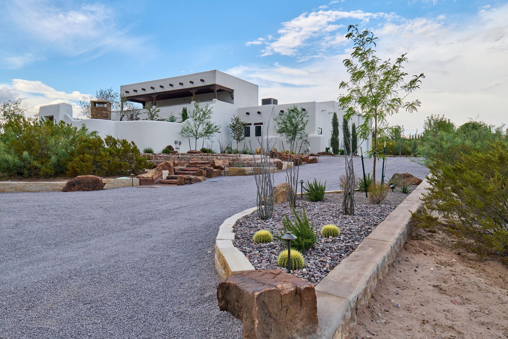 White stucco house with gravel driveway and desert landscaping under a blue sky.