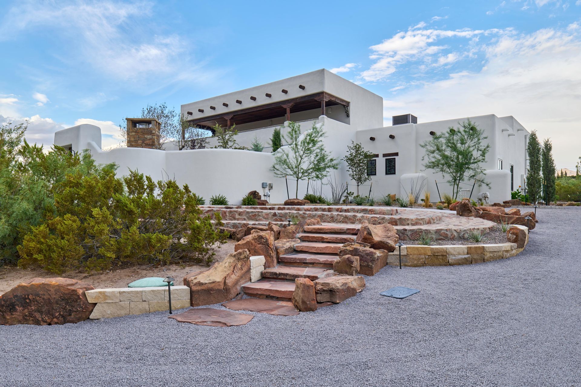 White stucco home with tiered rock landscaping and stairs.