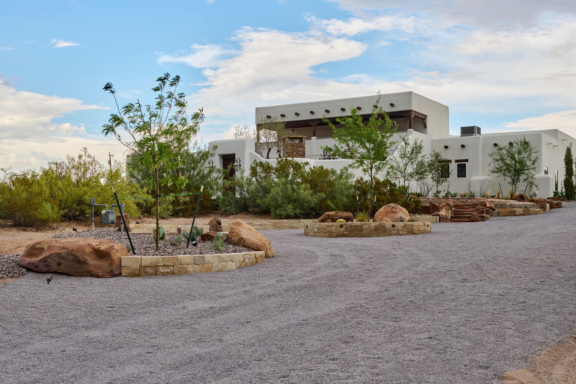 Southwestern style white building with a gravel driveway and desert landscaping under a blue sky.