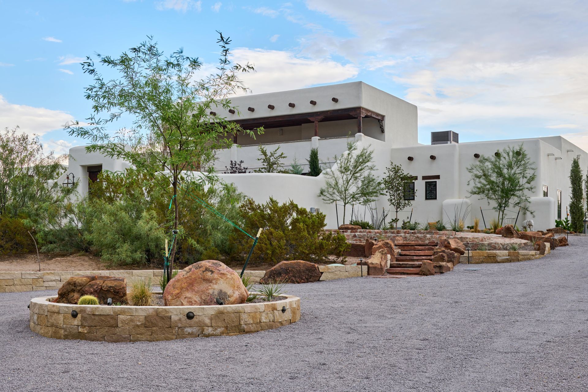 White stucco Southwestern-style house with gravel driveway, stone landscaping, and blue sky.