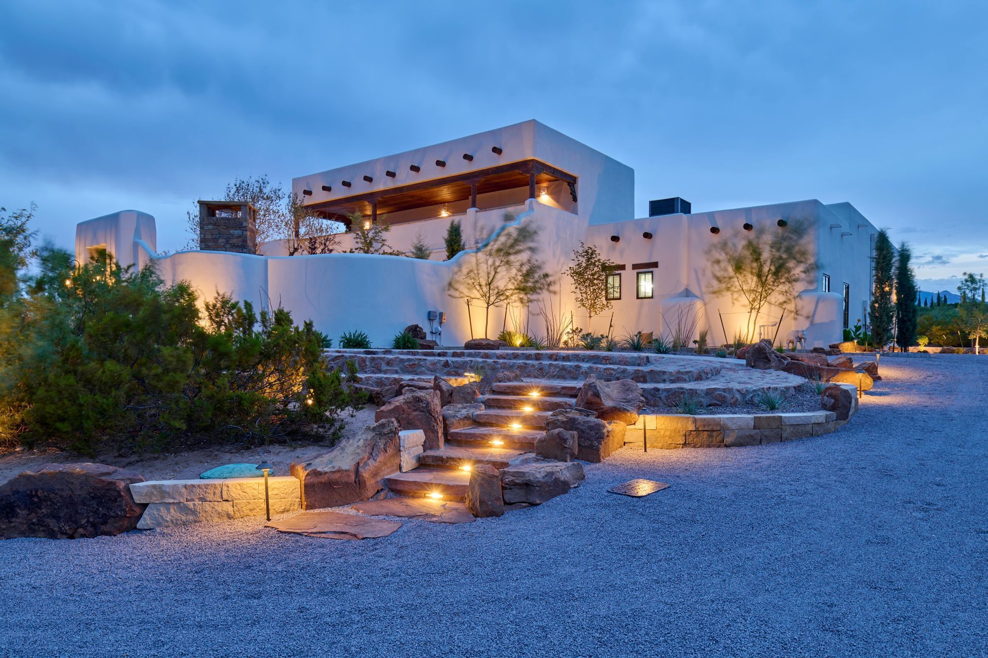 White stucco house with illuminated steps and landscaping at dusk.