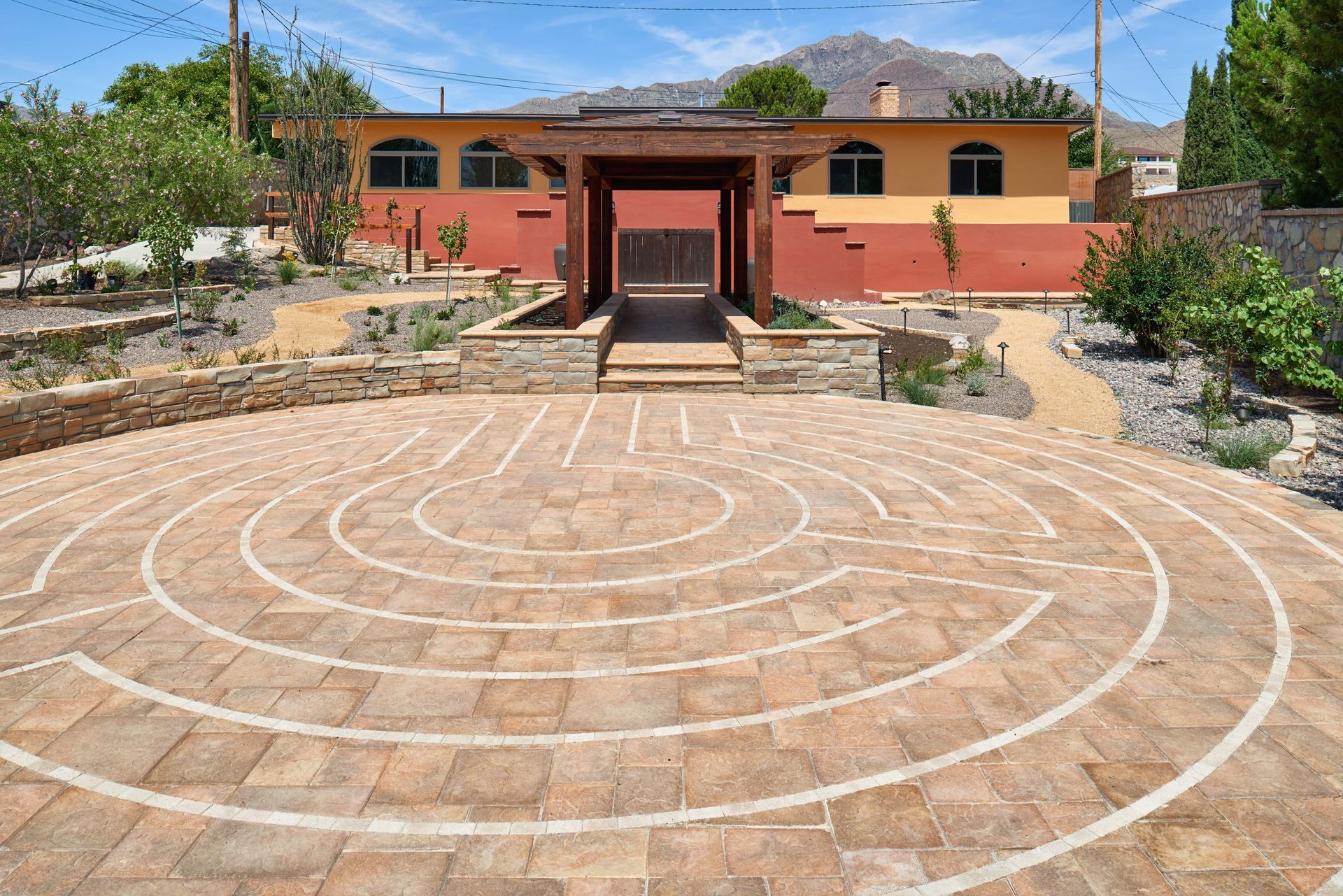 Circular brick labyrinth in front of a colorful building with a mountain backdrop.