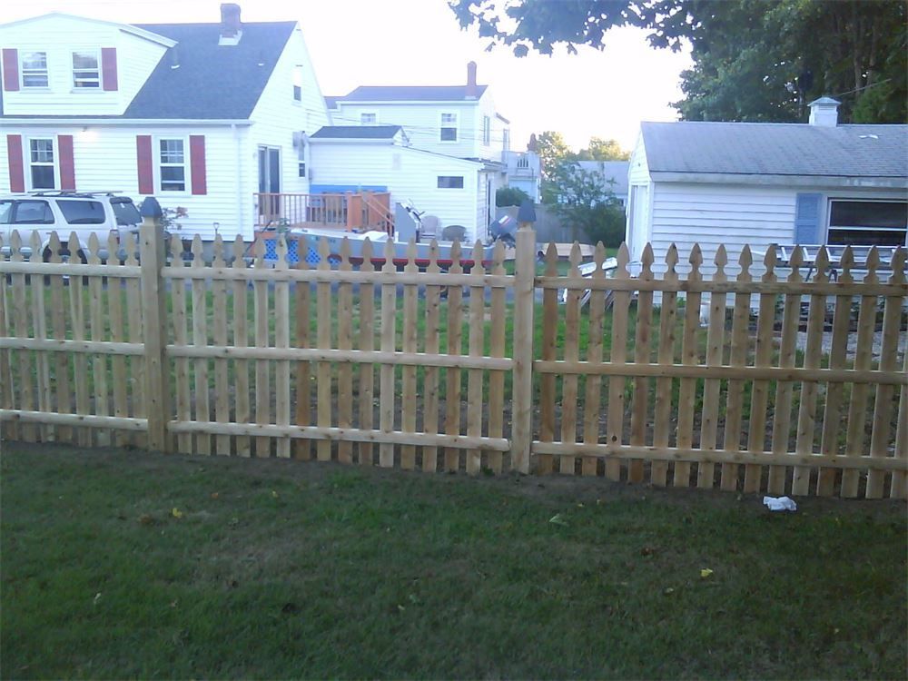 Wooden picket fence in a grassy yard, houses in the background.