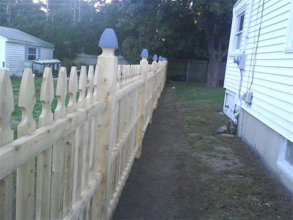Wooden picket fence with blue-topped posts runs along a lawn beside a white house.