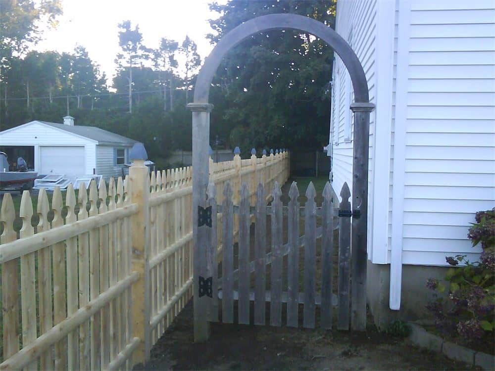 Wooden fence and gate with an arched top, leading into a yard.