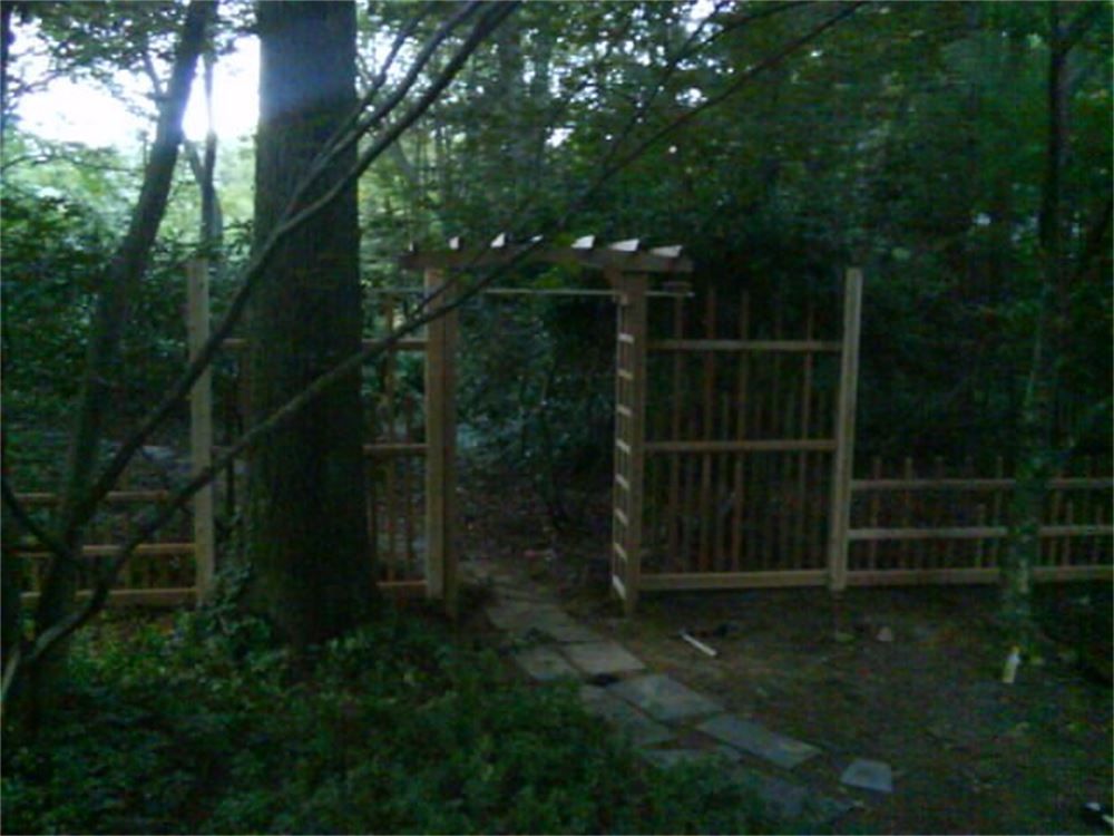 Wooden gate and fence with a stone path leading through a wooded area.