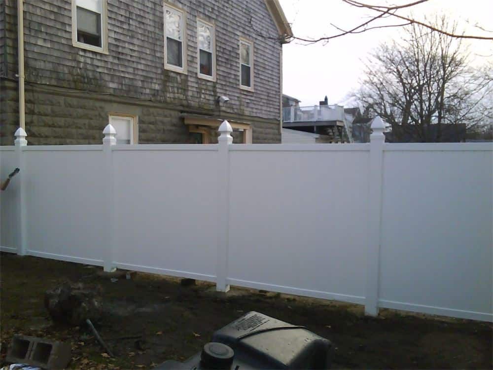 White vinyl privacy fence in front of a weathered gray building.