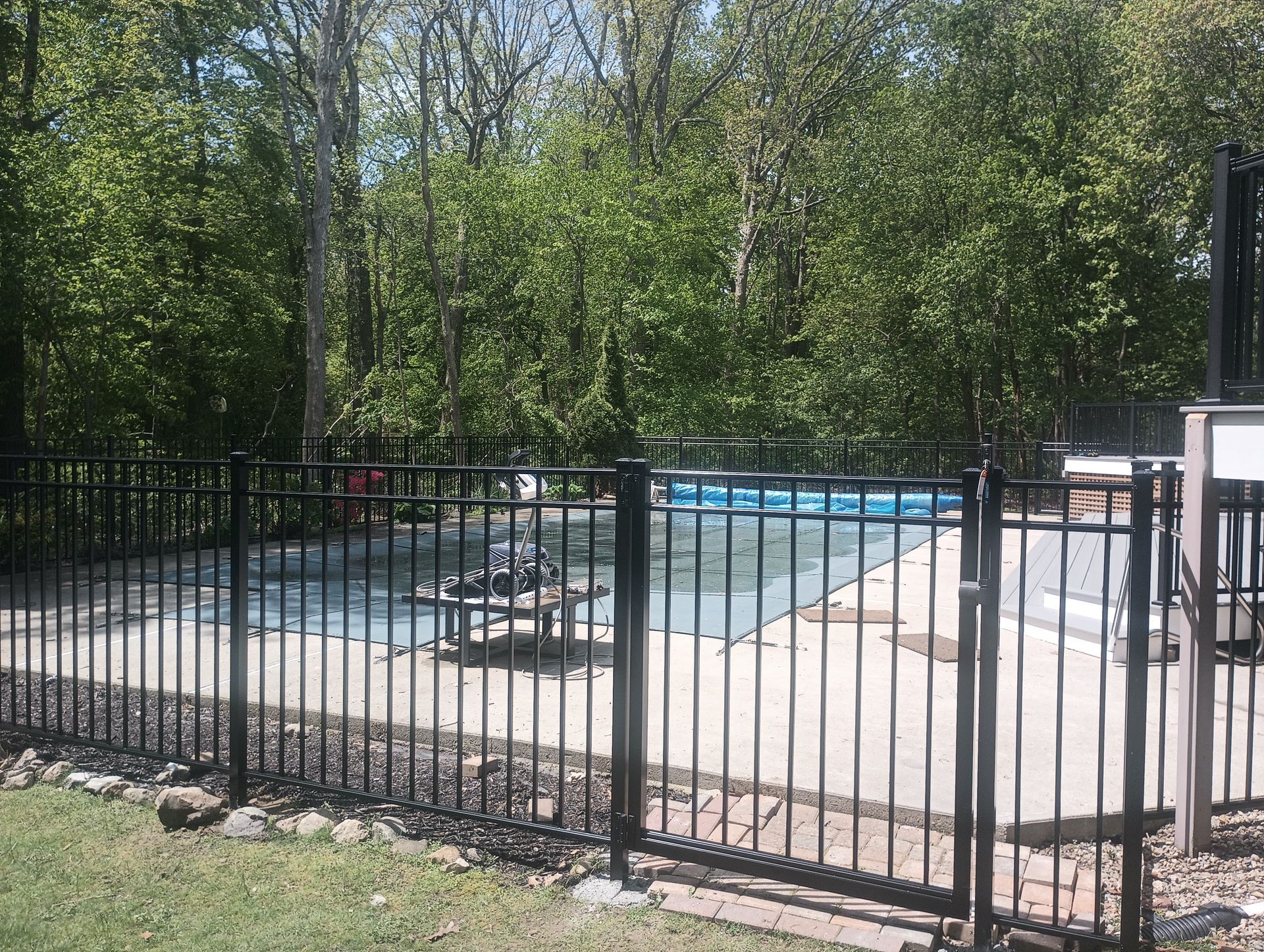 Black fenced-in outdoor swimming pool surrounded by trees.