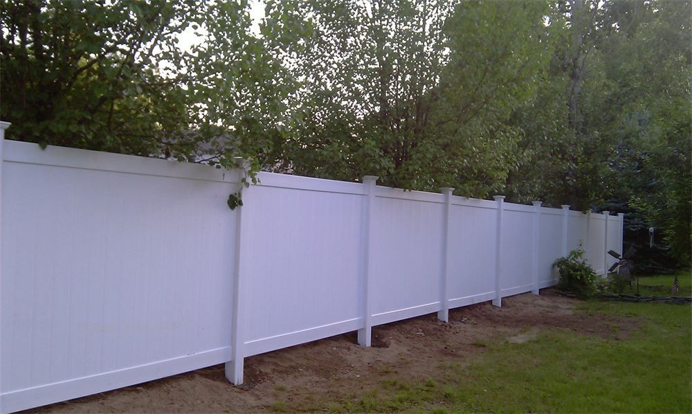 White vinyl privacy fence in a grassy yard, trees in the background.