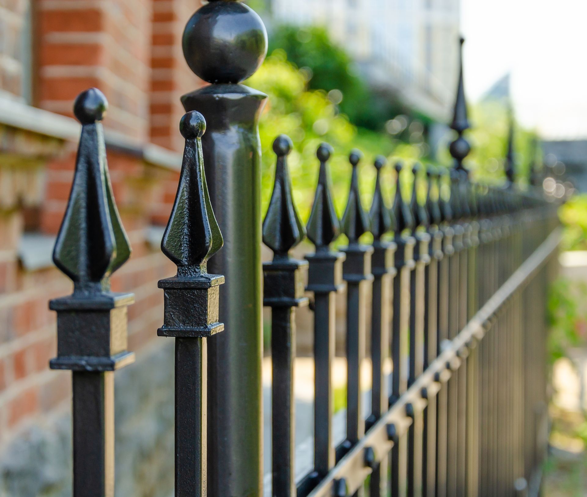 Black wrought iron fence with decorative spear-topped posts, in front of a brick building.