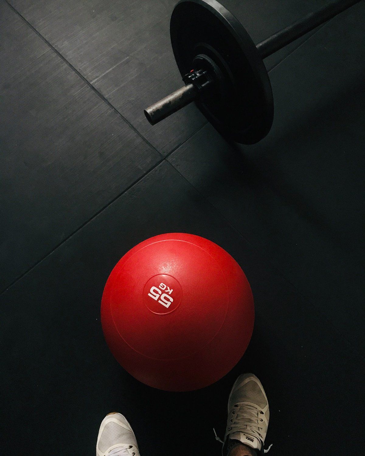 A person is standing next to a red ball and a barbell.