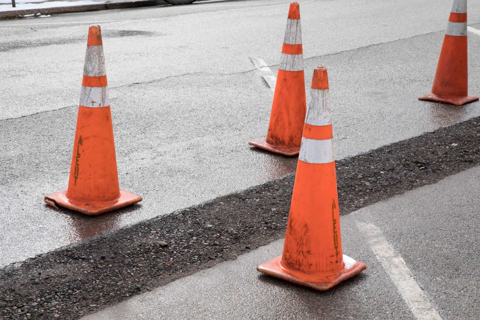 Orange traffic cones on wet asphalt, marking a road repair area.