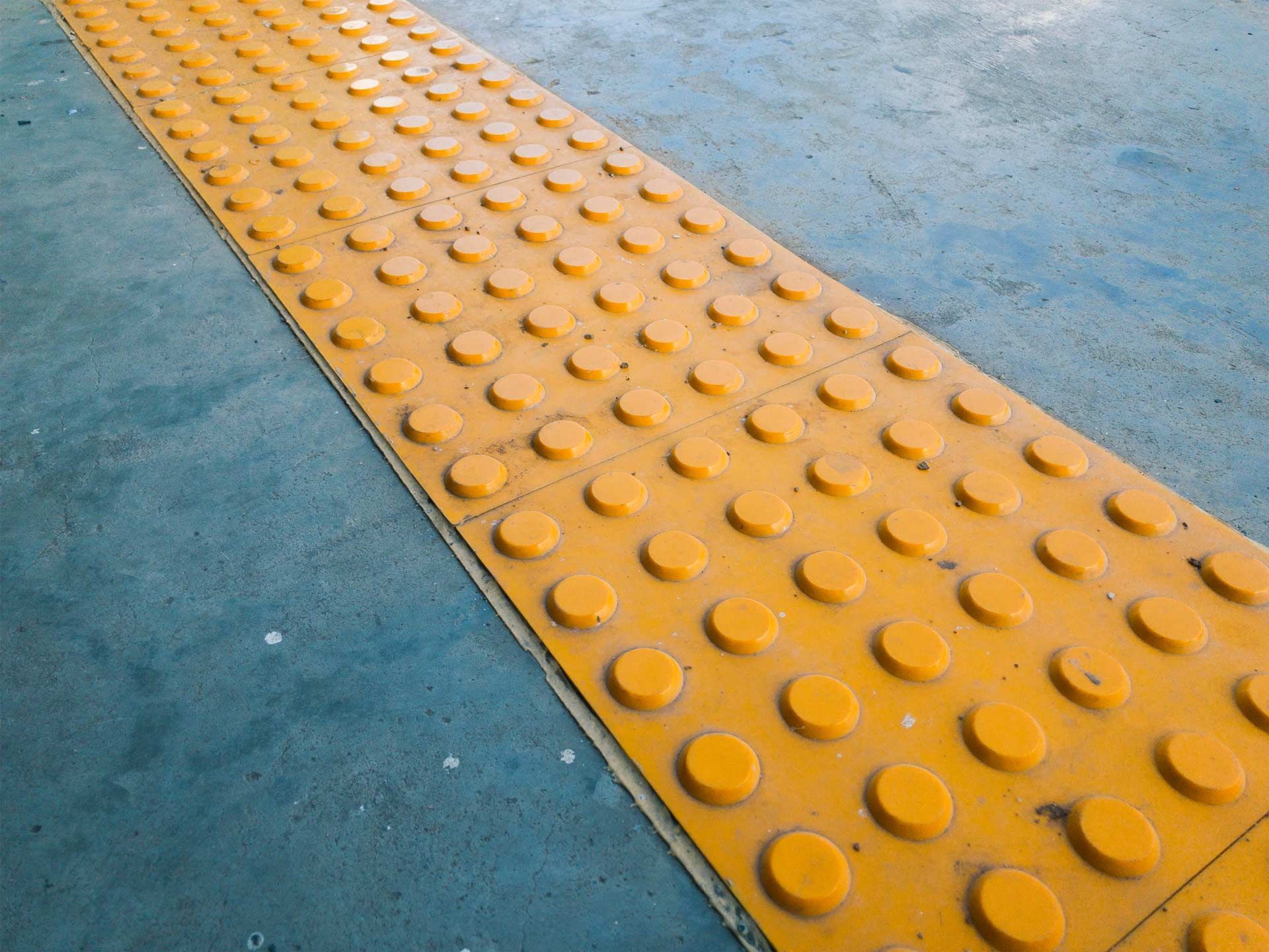 Yellow tactile paving with rounded bumps on a blue surface.