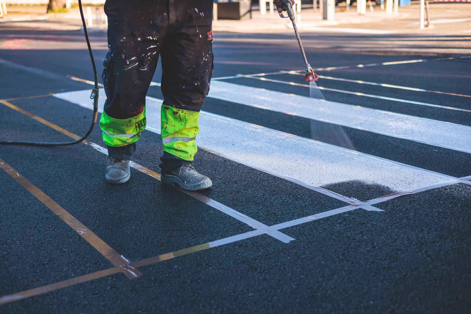 A person painting a white crosswalk with a spray gun on asphalt.