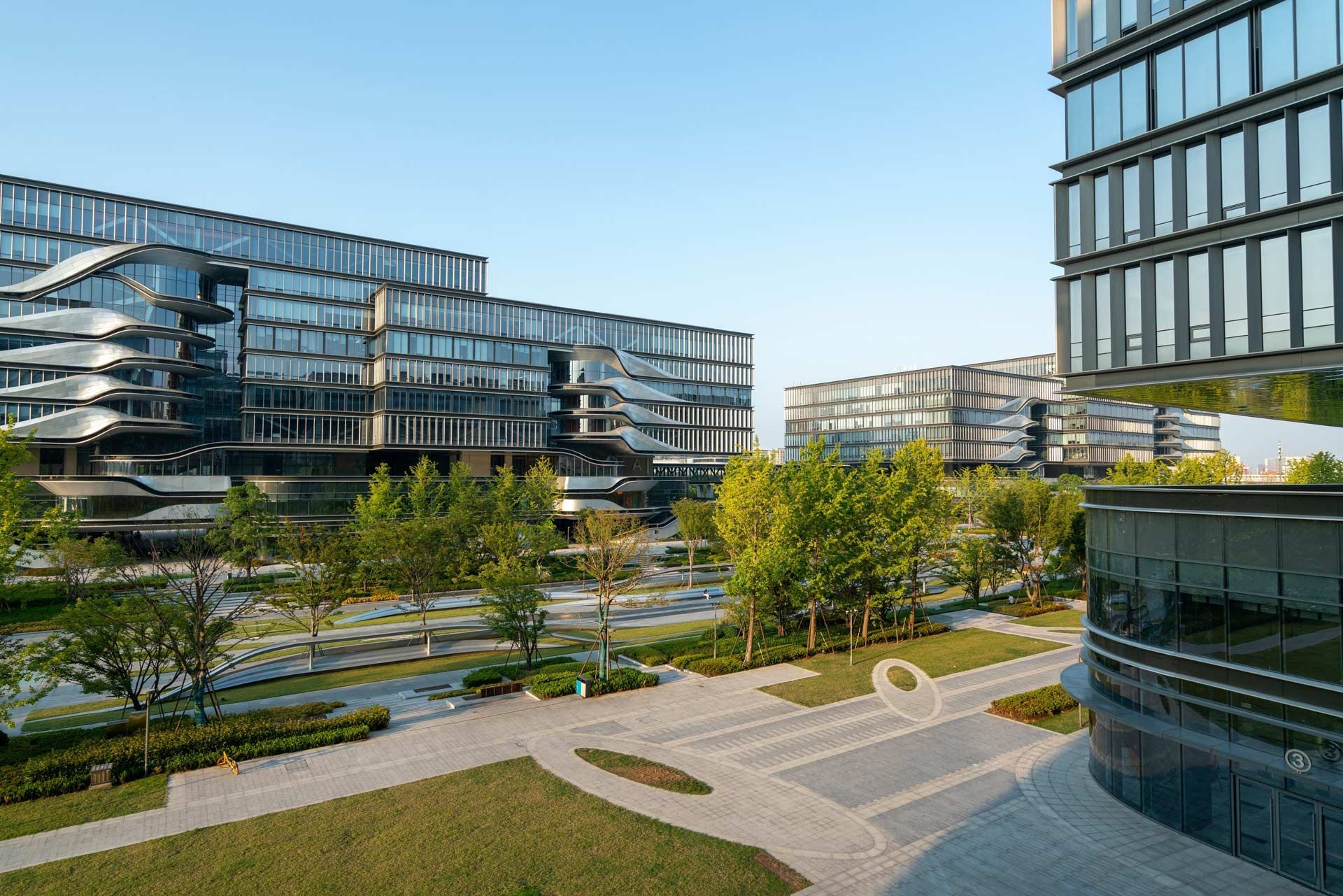 Modern glass buildings and green space with trees under a blue sky.