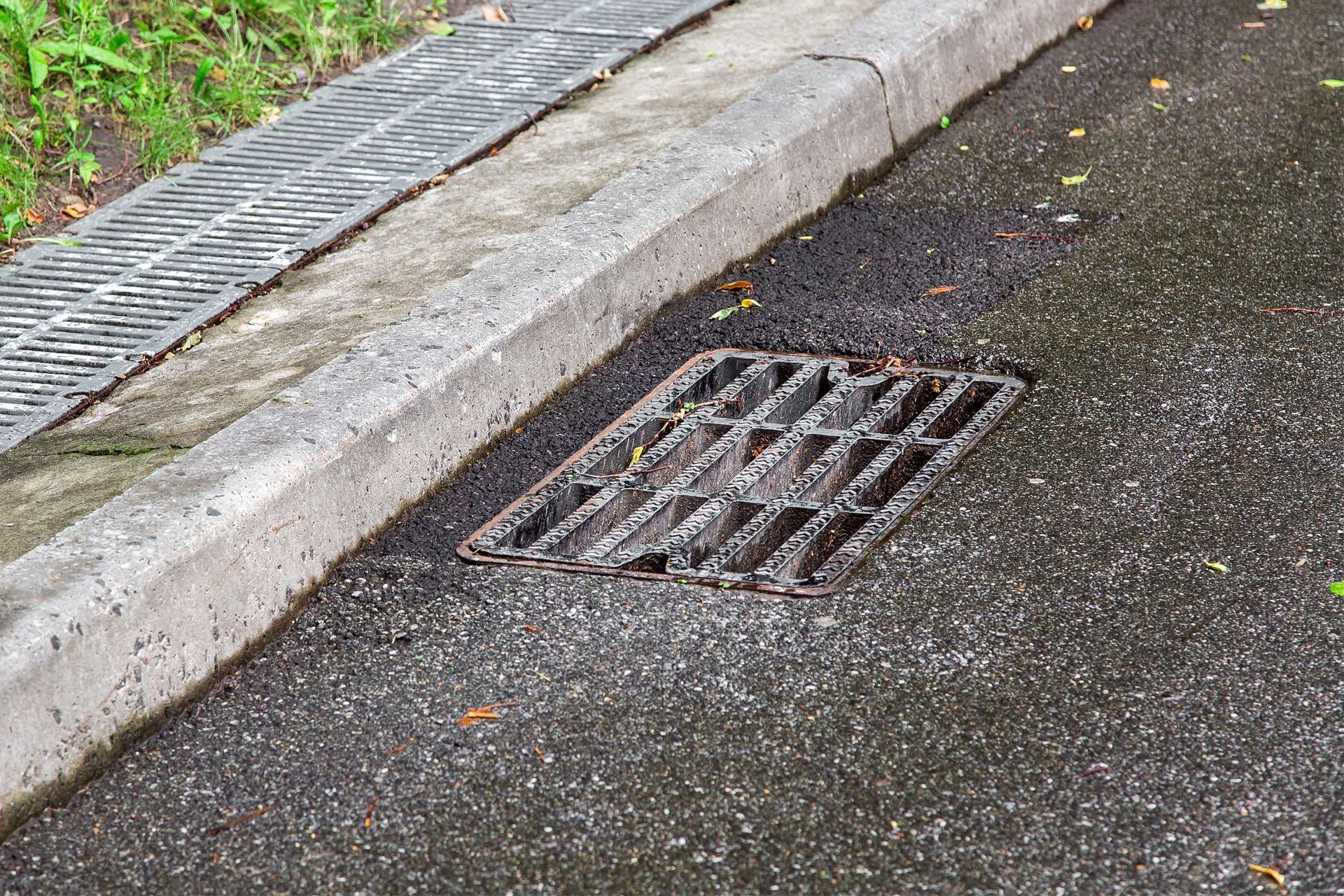 Asphalt road with a curb, a metal drain, and a gutter.