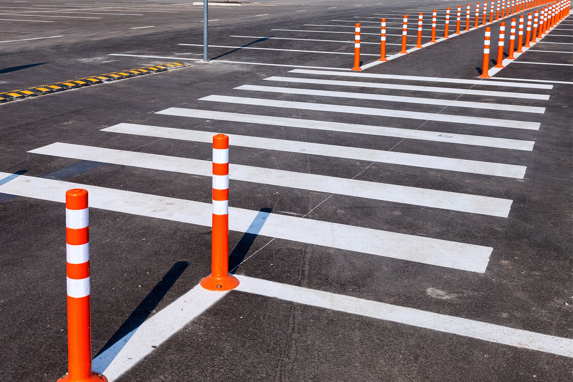 Crosswalk with orange and white bollards on asphalt.