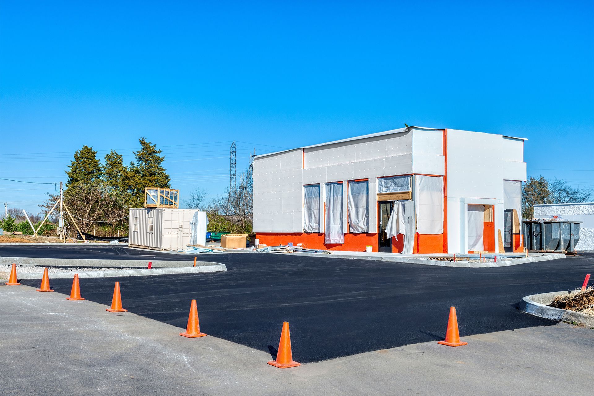 Orange and white building under construction with an empty parking lot and orange cones.