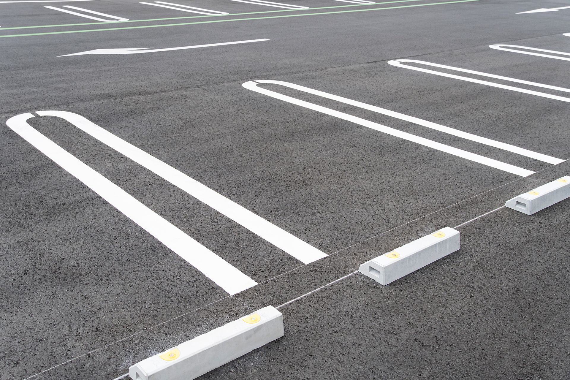 Parking spaces marked with white lines on asphalt, with parking bumpers at the end of each space.