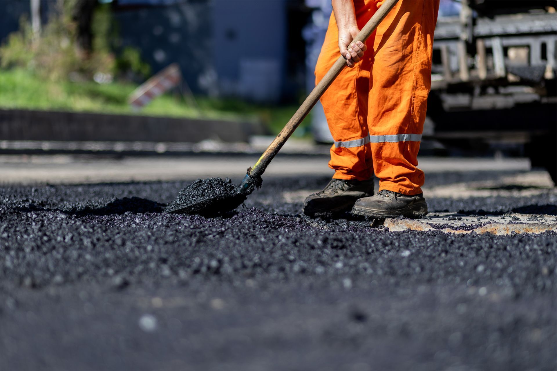Road worker in orange overalls raking asphalt on a street.