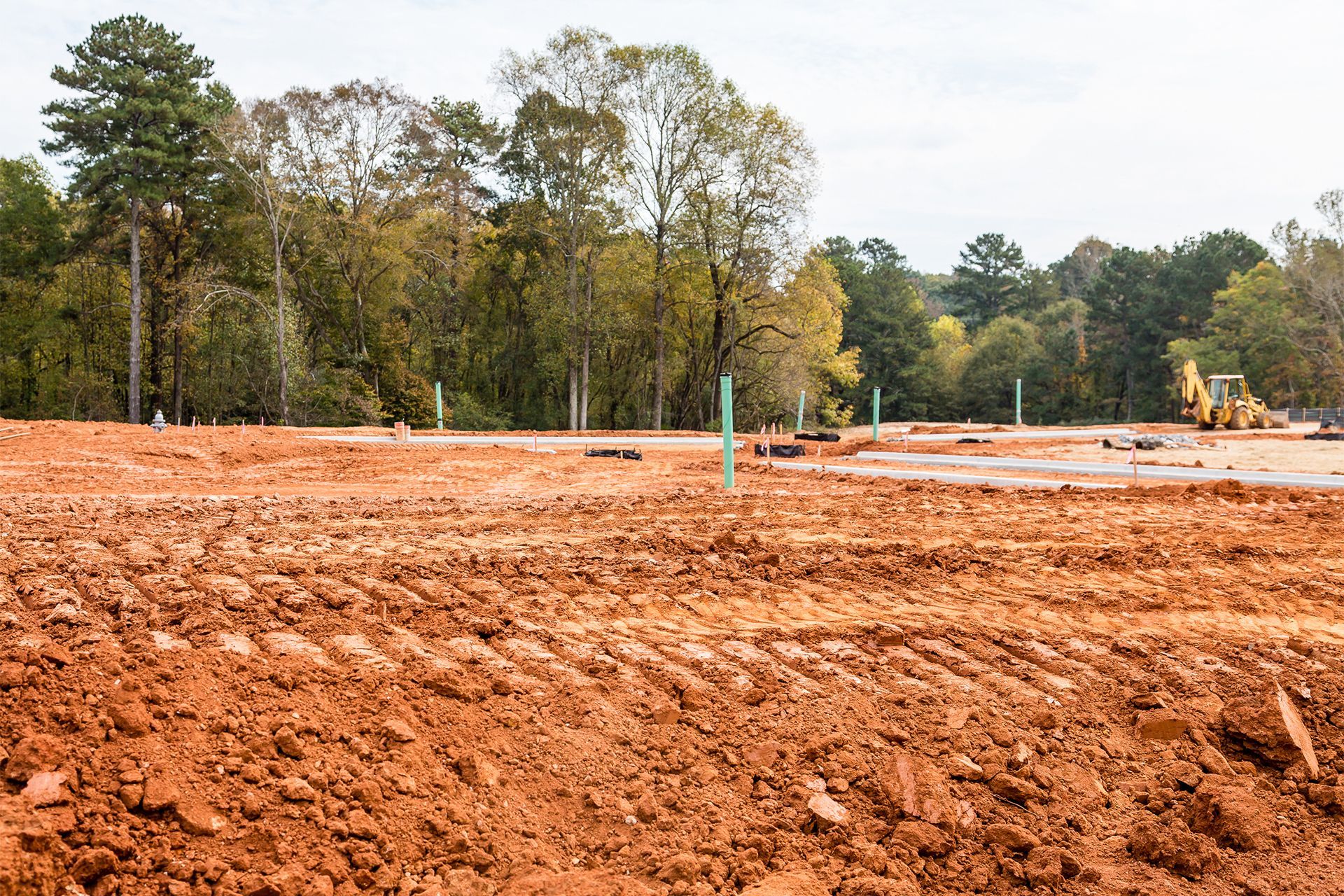 Construction site, red clay soil, green utility markers, trees in background.