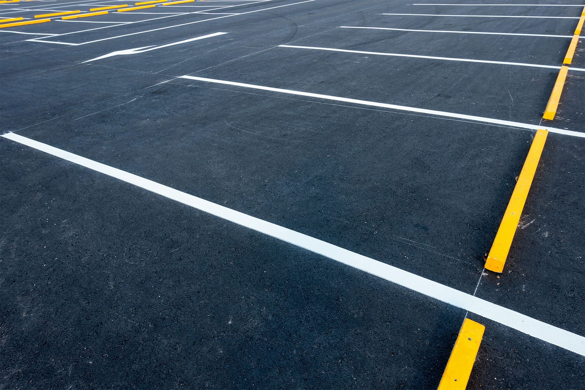 Empty asphalt parking lot marked with white and yellow painted lines.