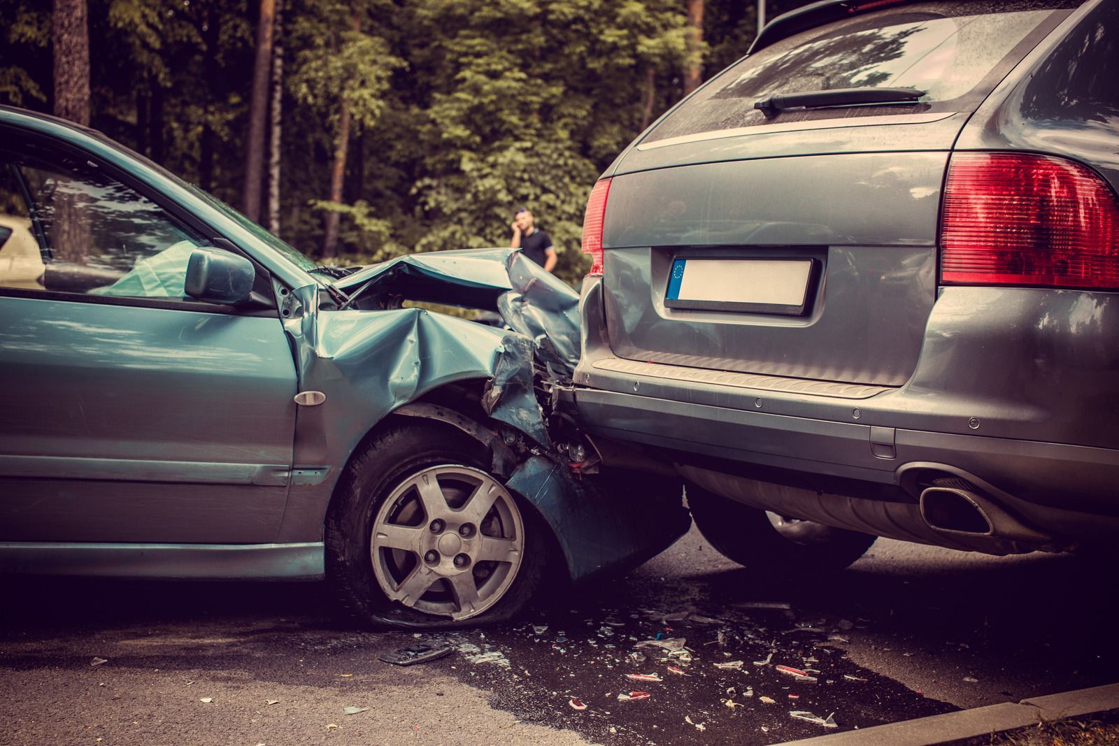 Two cars, one blue, one gray, crashed on a road with visible damage to both vehicles.