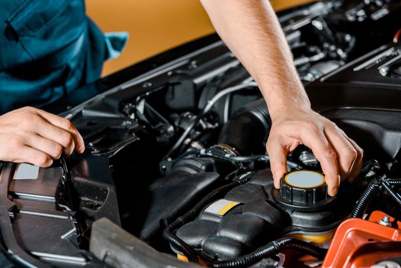 Mechanic opening car engine fluid cap. Black engine bay, focused on hand, orange, black, and grey.