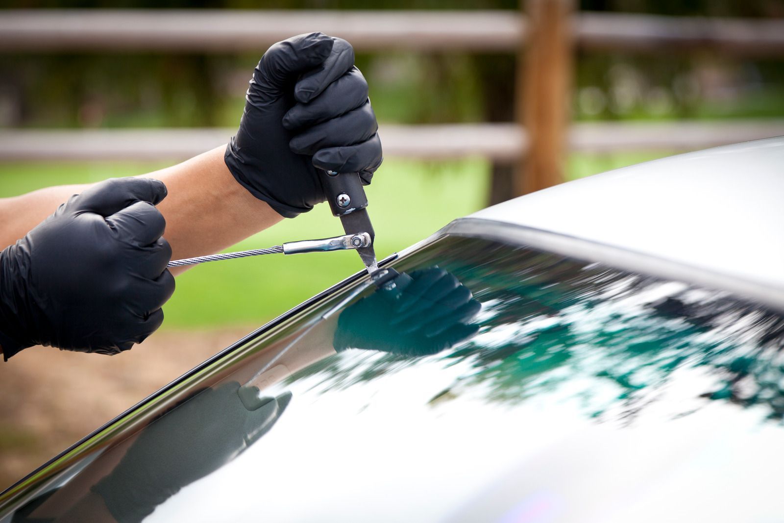 Hands in black gloves using a tool to trim black film from a car window.