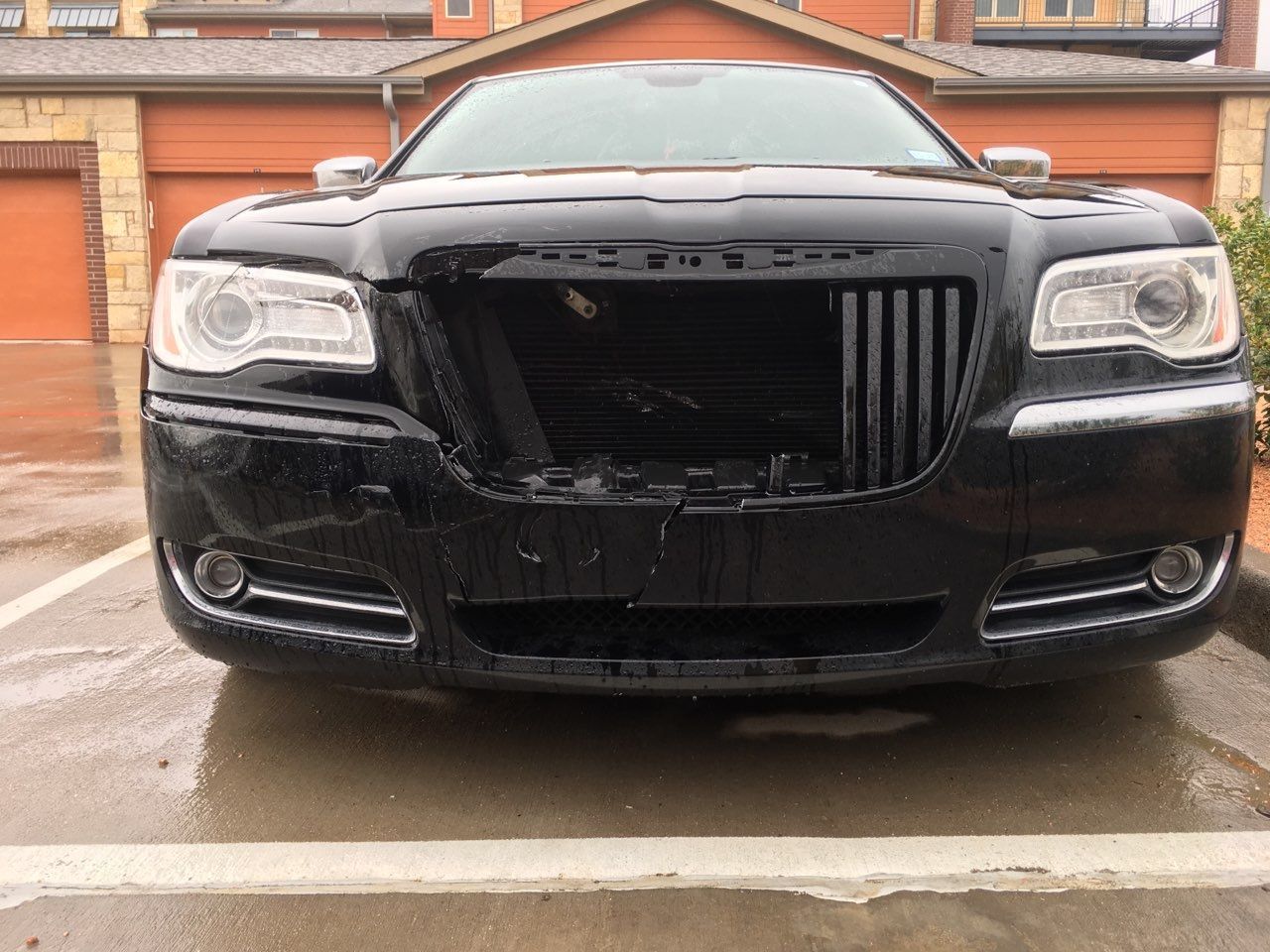Black Chrysler 300 with front bumper damage; parked outside a building.