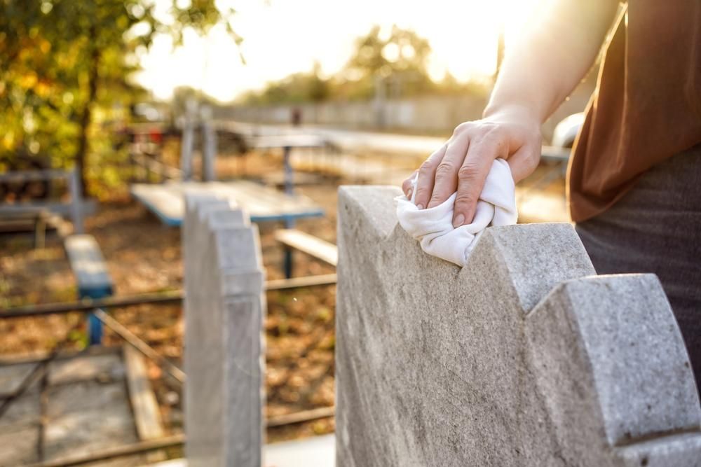A Person Is Cleaning a Gravestone with A Cloth in A Cemetery — Nick Locke Monuments in Bellingen, NSW