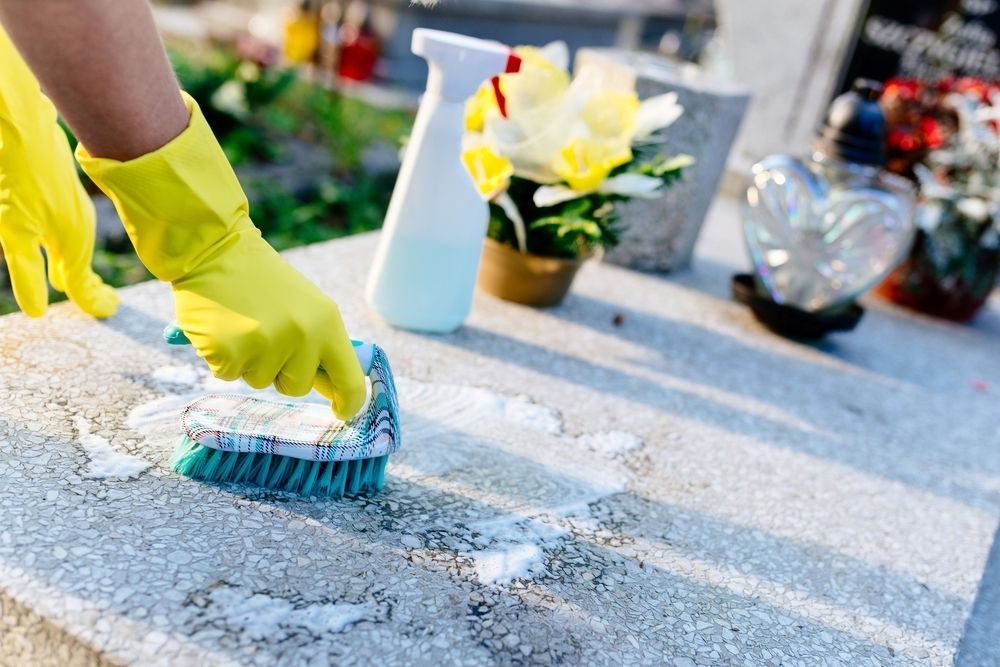 A Person Wearing Yellow Gloves is Cleaning a Grave With a Brush — Nick Locke Monuments in Dorrigo, NSW