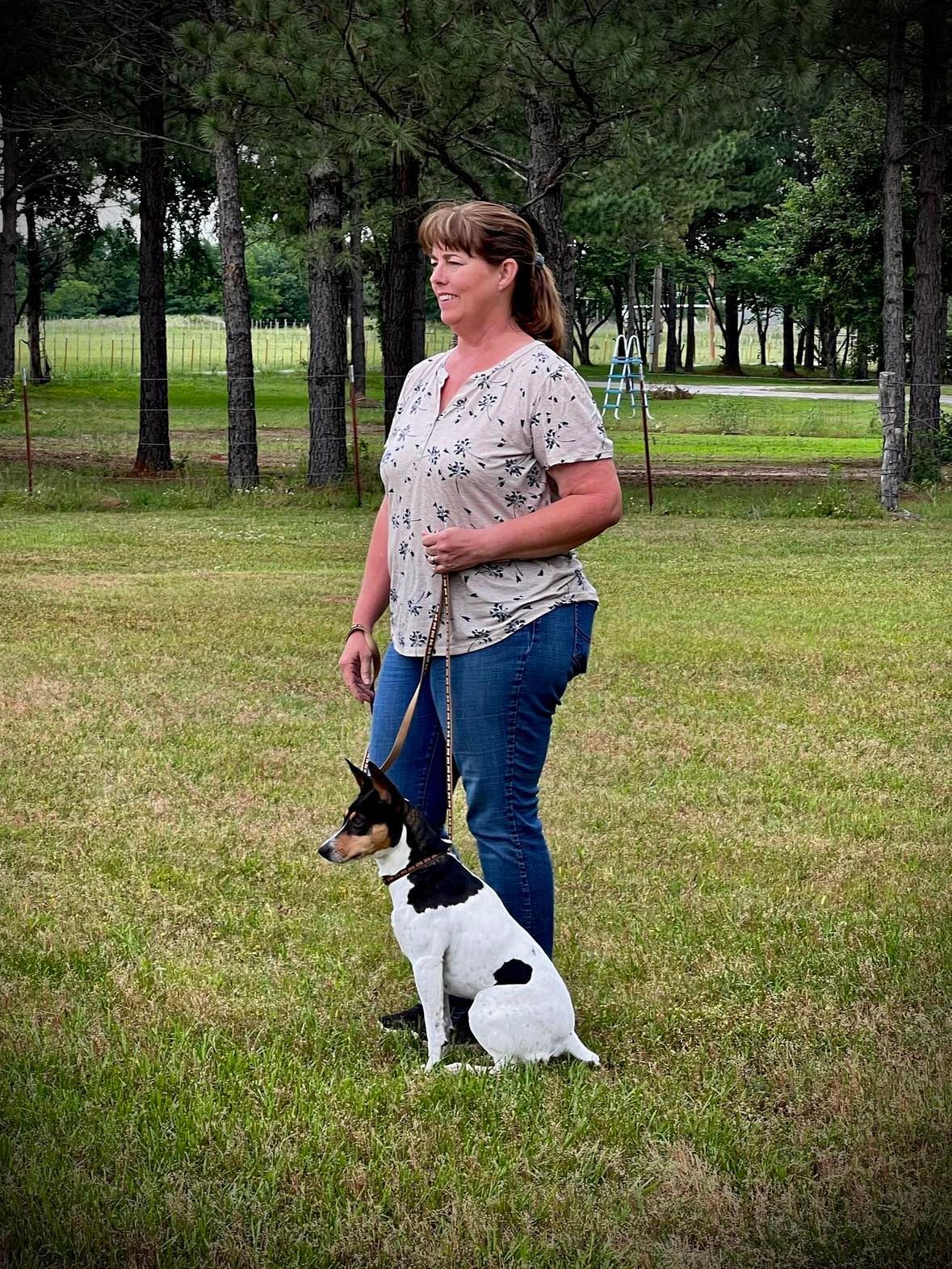 A woman is walking a small dog on a leash in a field. A woman is walking a small dog on a leash in a field.