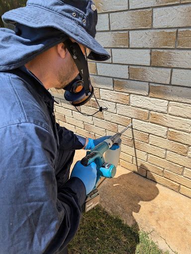 A Man is Spraying a Brick Wall With a Sprayer — Total Pest and Carpet Cleaning in Kinka Beach, QLD