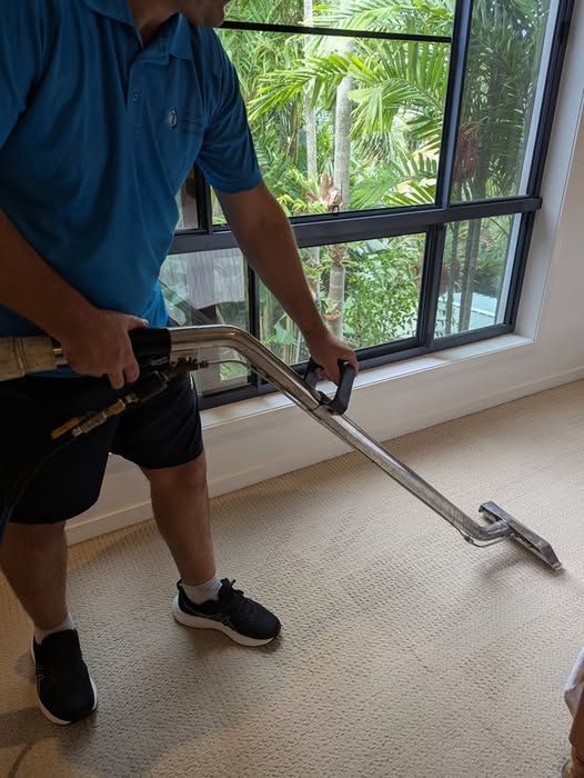 A Man is Cleaning a Carpet With a Vacuum Cleaner — Total Pest and Carpet Cleaning in Kinka Beach, QLD